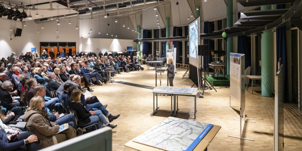 Mehrere Gäste die sich im voll besetzten Saal den Masterplan erklären lassen