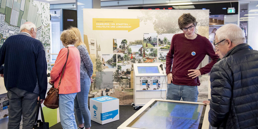 Besucher:innen der Ausstellung, 5 Personen, die im Gespräch sind und sich die Ausstellung ansehen
