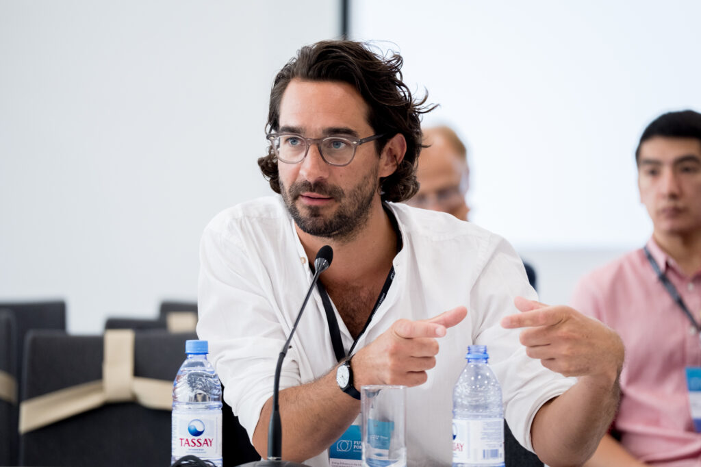 Max Schwitalla von Studio Schwitalla sitzt an einem Tisch und spricht in ein Mikrofon