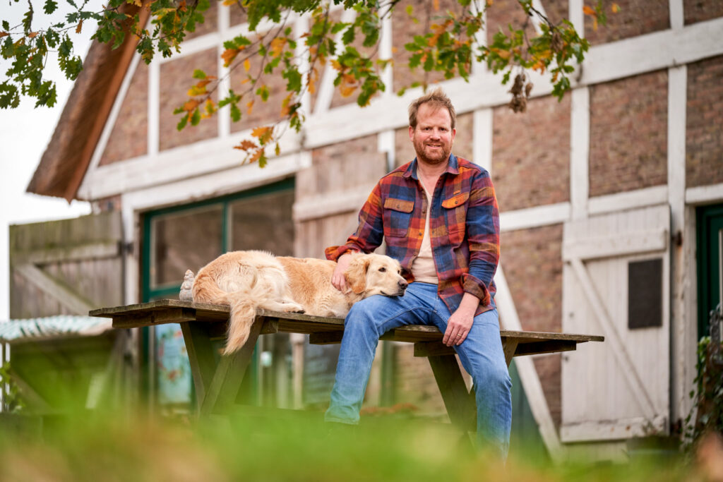 Mann mit Hund vor Bauernhaus