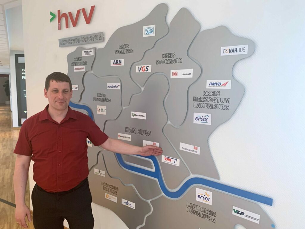 Ein Mann steht vor einer Karte der Metropolregion hamburg und den Logos der jeweiligen Verkehrsunternehmen
