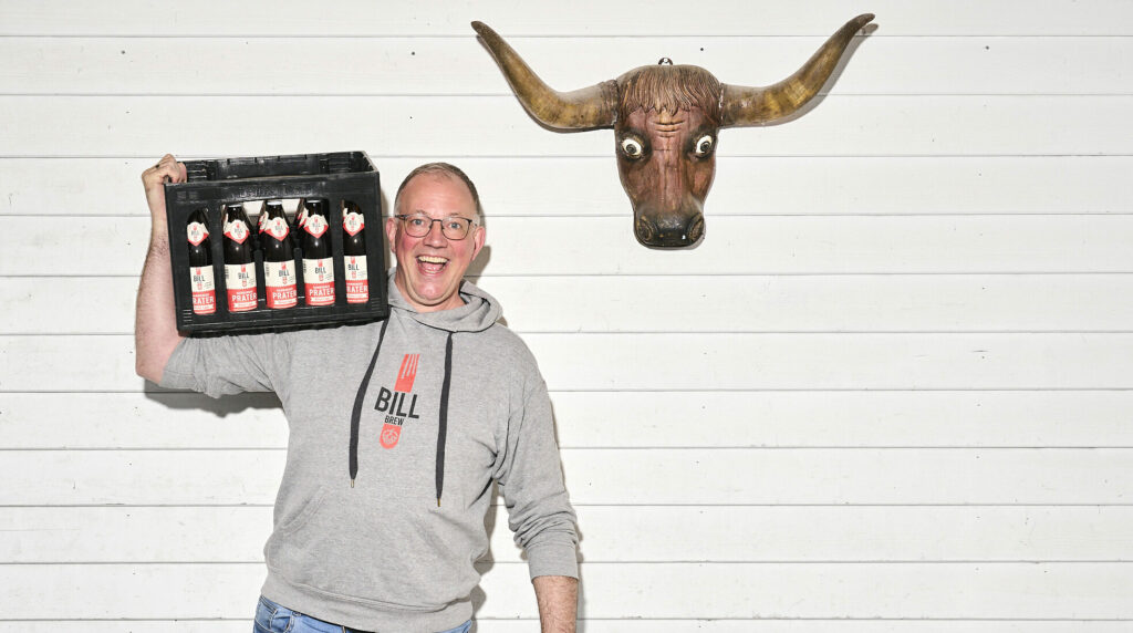 Christian Temme mit einem Bierkasten auf der Schulter, neben ihm hängt ein Stierschädel an der Wand