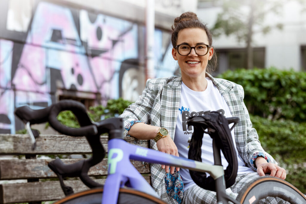 Podcast-Gästin Katja Diehl sitzt auf einer Bank, vor ihr im Anschnitt ein Fahrrad